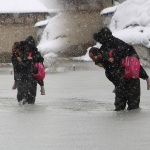 Evinin önünde biriken su nedeniyle çocuklarını sırtında taşıyor